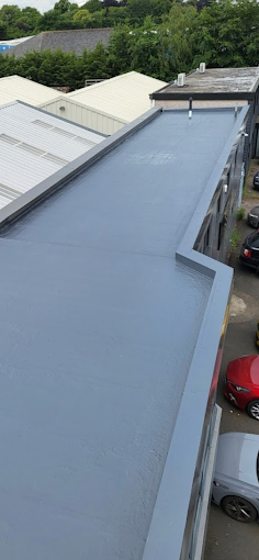 Flat gray roof on a commercial building with parked cars below
